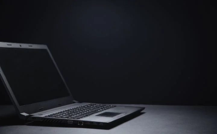 Na czarnym tle leży otwwarty wyłączony laptop