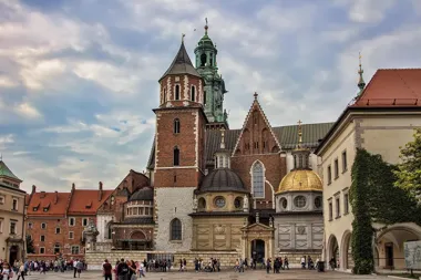 Katedra na Wawelu z wieżami i kopułami, przed nią spacerują turyści na placu.