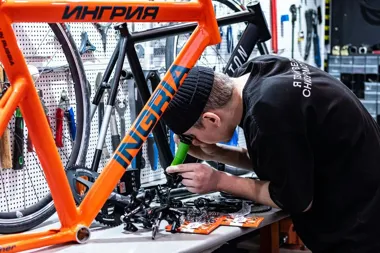 Mechanik serwisuje pomarańczową ramę roweru na stole warsztatowym.
