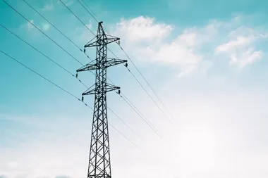 Słup wysokiego napięcia z liniami energetycznymi na tle nieba z chmurami.