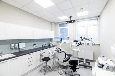 Nowoczesny gabinet stomatologiczny z fotelem dentystycznym, lampą zabiegową i szafkami.
