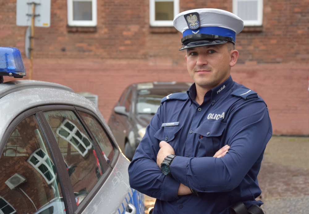 sierżant Sebastian Fluder stoi przy radiowozie na dziedzińcu komendy miejskiej