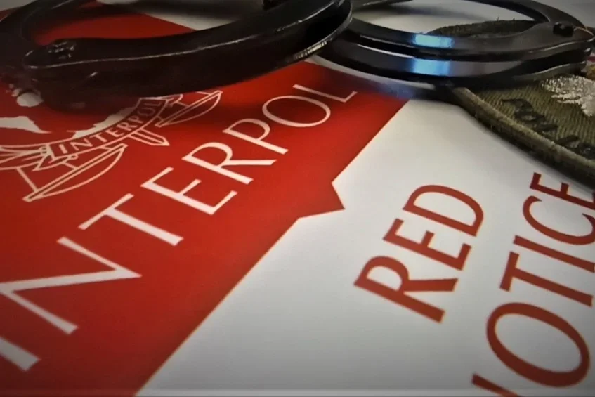 Kajdanki leżą na dokumencie Interpolu z napisem „Red Notice”.
