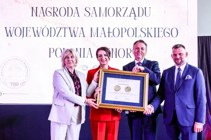 Cztery osoby na scenie trzymają dużą ramę z dyplomem podczas uroczystości wręczenia Nagrody Samorządu Województwa Małopolskiego Polonia Minor.