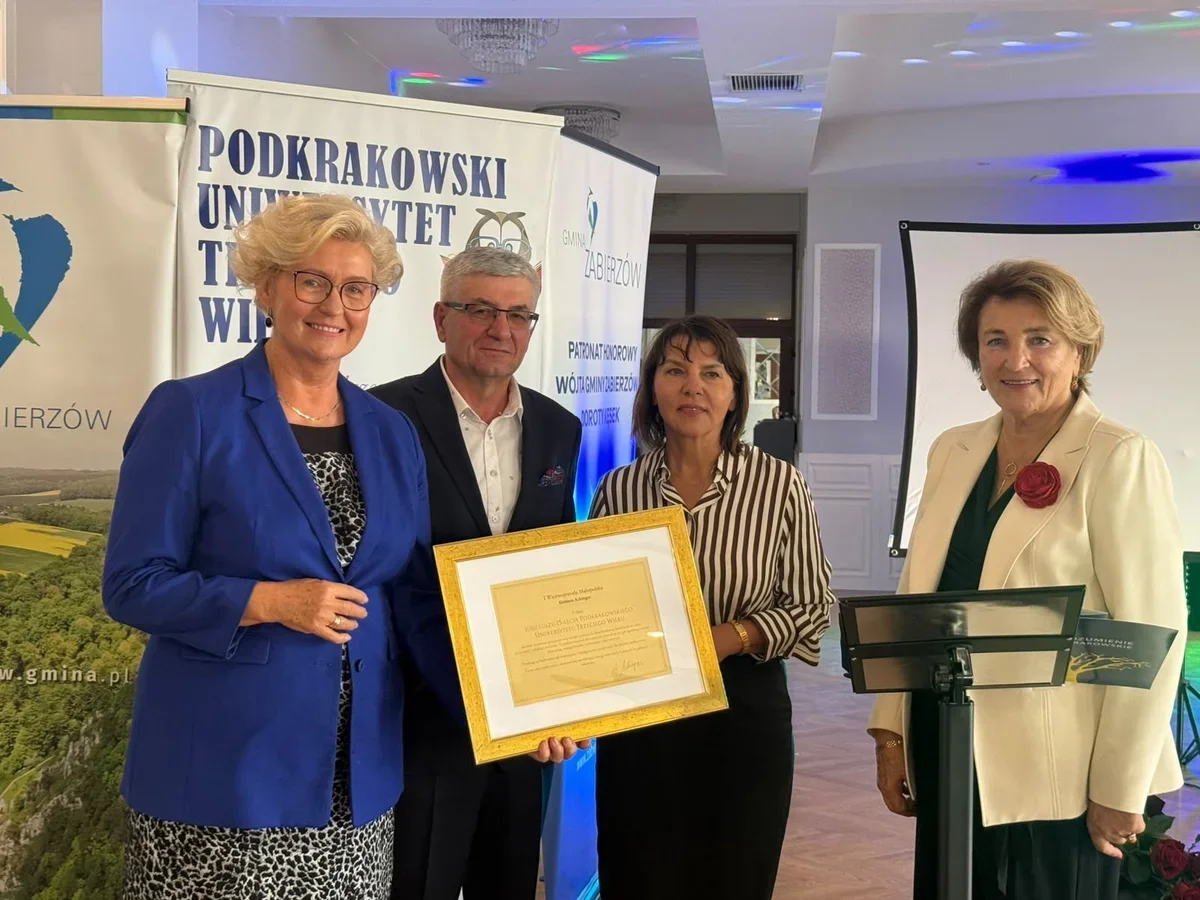 Cztery osoby pozują z okazją w ramach wydarzenia Podkrakowskiego Uniwersytetu Trzeciego Wieku w Zabierzowie, jedna z nich trzyma uhonorowaną dyplomem w złotej r