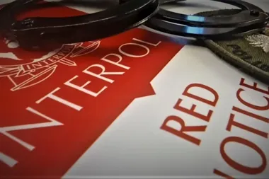 Kajdanki leżą na dokumencie Interpolu z napisem „Red Notice”.