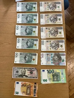 Na drewnianym stole ułożone są stosy banknotów o nominałach 100, 200 i 500 złotych, 50 dolarów oraz 50 i 100 euro.