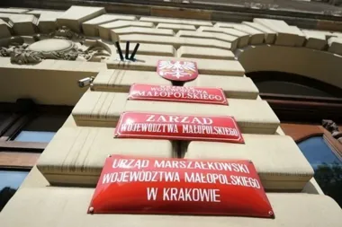 Czerwone tablice z nazwami urzędów województwa małopolskiego na elewacji budynku w Krakowie.