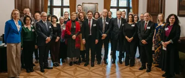 Grupa osób w eleganckim, historycznym wnętrzu z drewnianą boazerią i dużymi oknami pozuje do zbiorowego zdjęcia.