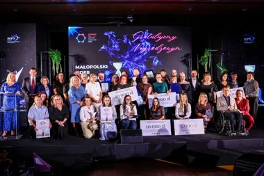 Grupa osób pozuje na scenie podczas gali wręczenia nagród Małopolski Lider Ekonomii Społecznej 2026, uczestnicy trzymają czeki i dyplomy.