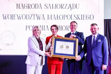 Cztery osoby na scenie trzymają dużą ramę z dyplomem podczas uroczystości wręczenia Nagrody Samorządu Województwa Małopolskiego Polonia Minor.