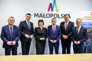 Sześć osób w garniturach pozuje do zdjęcia przed ścianą z logo województwa małopolskiego.