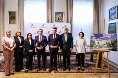 Grupa siedmiu osób pozuje do zdjęcia w reprezentacyjnym pomieszczeniu z banerem Małopolski, obok stojaka z wizualizacją budynku.