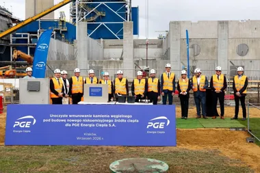 Grupa osób w kamizelkach ochronnych i kaskach stoi na terenie budowy nowego źródła ciepła PGE Energia Ciepła w Krakowie podczas uroczystości wmurowania kamienia