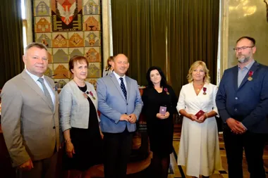 Grupa osób w eleganckim wnętrzu z odznaczeniami i dyplomami podczas uroczystości wręczenia wyróżnień.