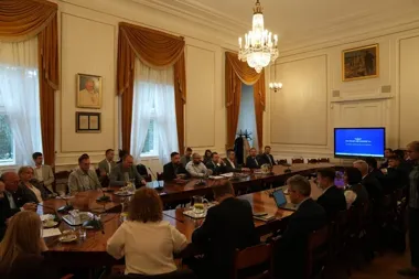 Uczestnicy spotkania biznesowego związanego z PKP Polskie Linie Kolejowe S.A. siedzą przy dużym drewnianym stole w reprezentacyjnej sali konferencyjnej.