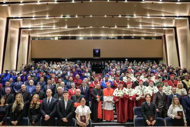 Uroczyste grupowe zdjęcie uczestników akademickiej lub kościelnej ceremonii w nowoczesnej auli.
