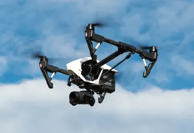 Dron z kamerą lata na tle błękitnego nieba z białymi chmurami.
