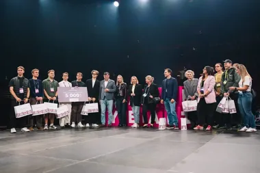 Grupa osób stoi na scenie podczas uroczystego wręczenia nagrody w postaci czeku na 5000 zł i toreb upominkowych.